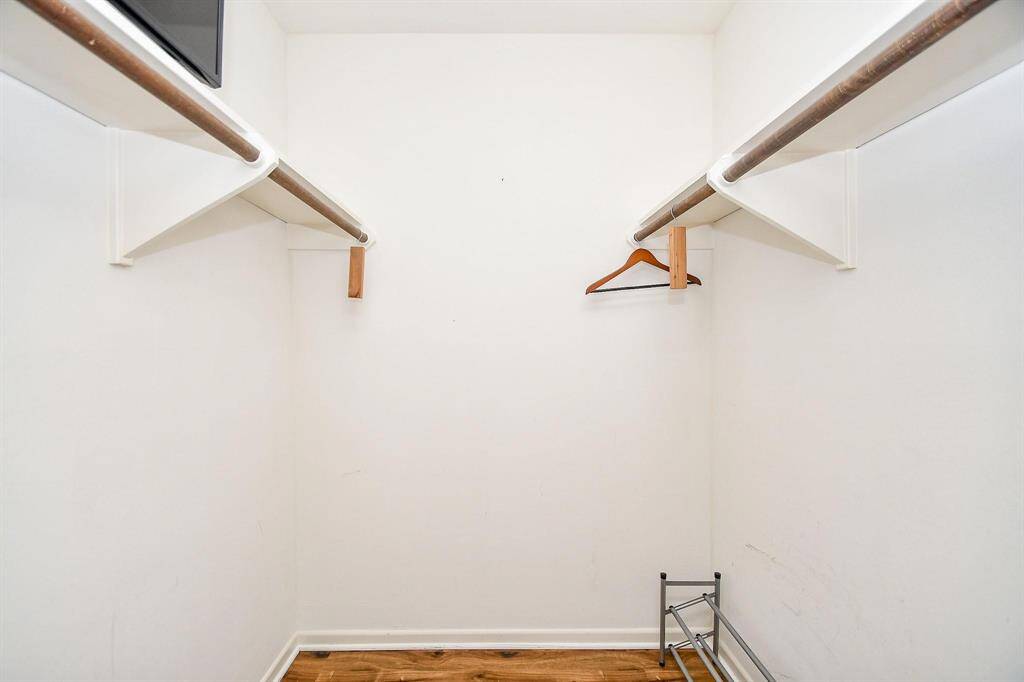 Spacious walk-in closet with white walls, wooden flooring, and dual hanging rods for clothing.