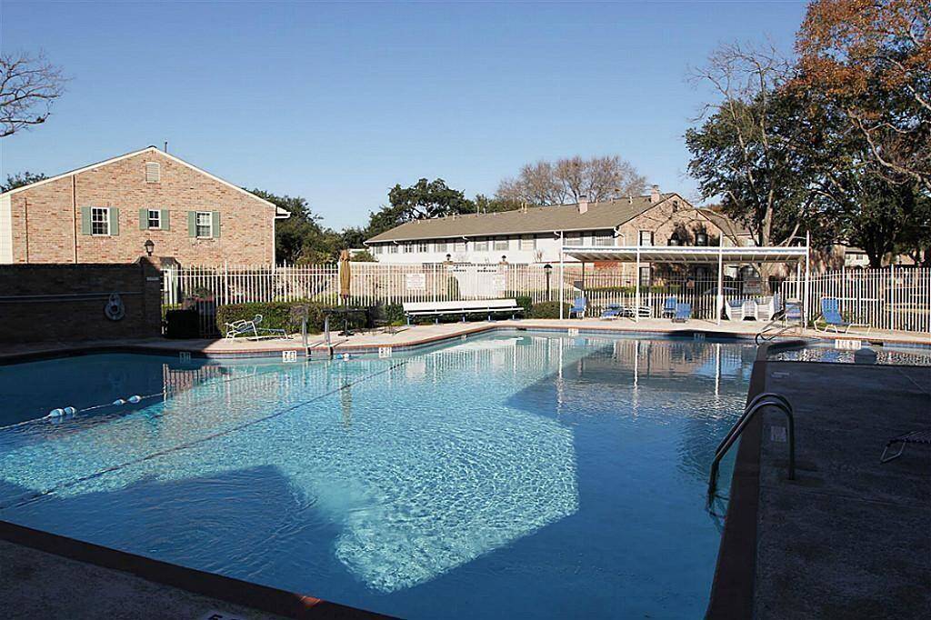 Well-maintained, spacious swimming pool in the neighborhood, surrounded by a fence and situated adjacent to brick buildings. Perfect for relaxation and leisure activities.