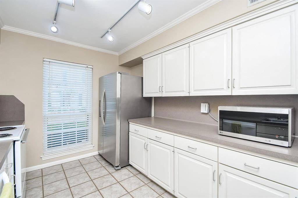 Tons of storage space, a sleek stainless steel refrigerator, and a built-in microwave. It has a clean, neutral color palette with tiled flooring and track lighting, creating a bright and inviting space.