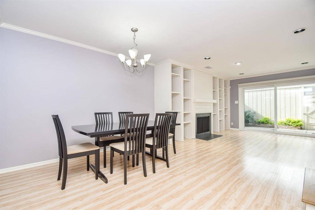 This spacious dining and living area features a modern light fixture and built-in shelving surrounding a cozy fireplace. Large sliding glass doors provide ample natural light and access to the outdoors.