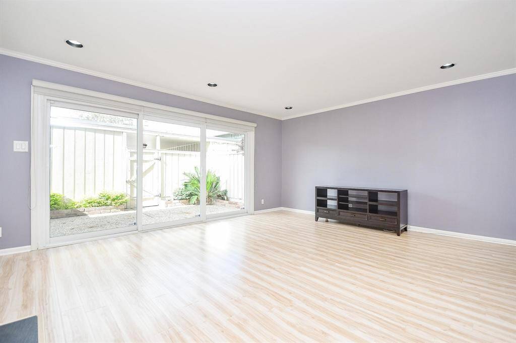 Spacious living room with Large sliding glass doors open to a small patio with greenery, enhancing natural light. Simple ceiling spotlights add sleek elegance.