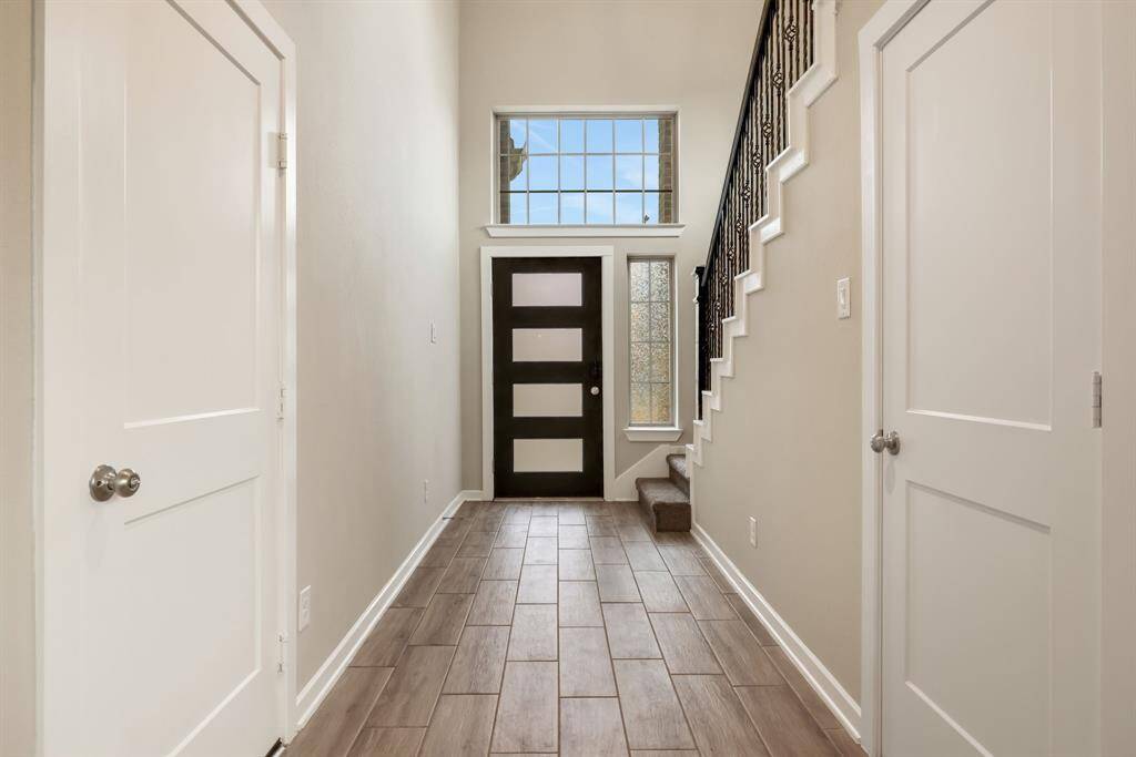 Two story entryway with wood looking tiled floors and a modern sleek front door