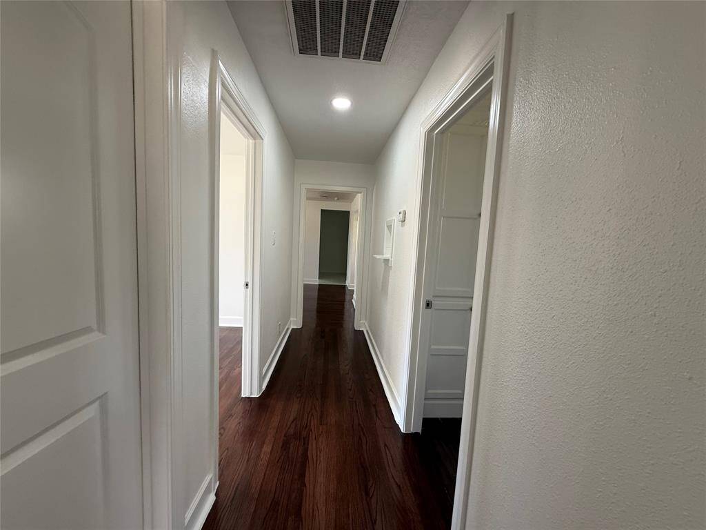 This photo shows a bright, narrow hallway with white walls and dark hardwood flooring. It has multiple doors leading to other rooms, creating a sense of openness and connectivity in the home.