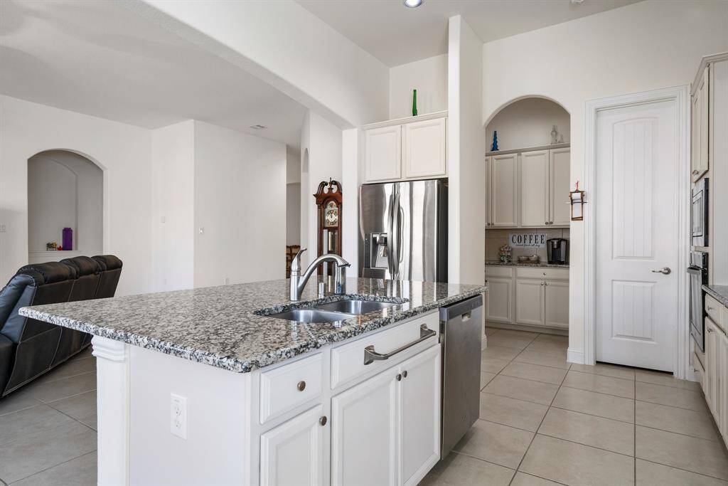Modern kitchen features sleek white cabinetry, granite countertops, and a spacious island with a built-in sink.