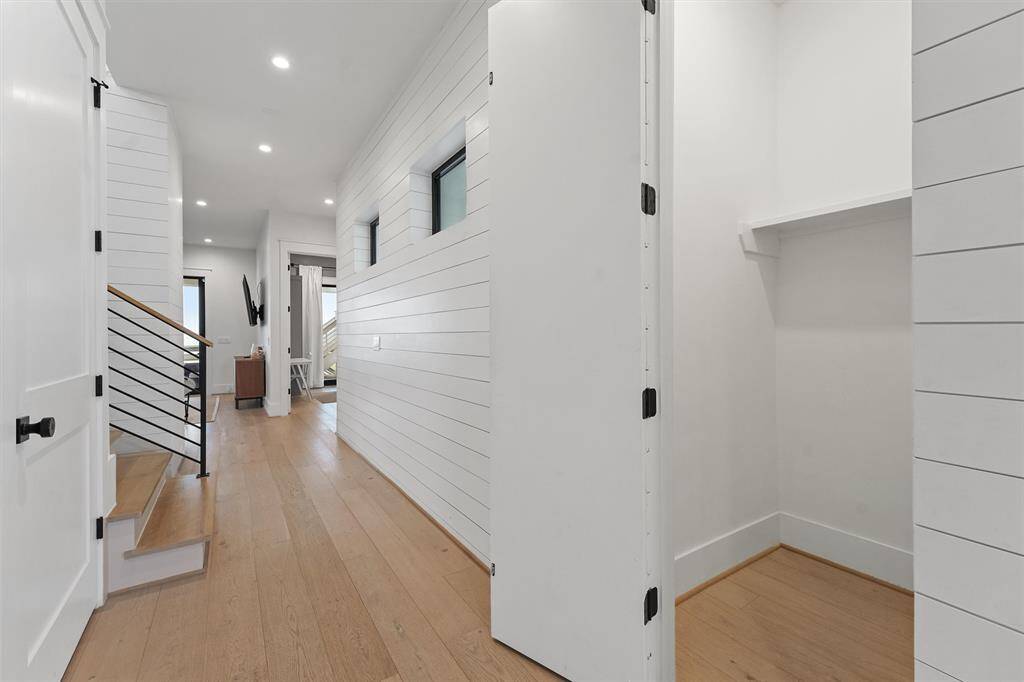 Bright and airy entry hallway with shiplap walls, warm wood flooring, and hidden door with extra storage space.