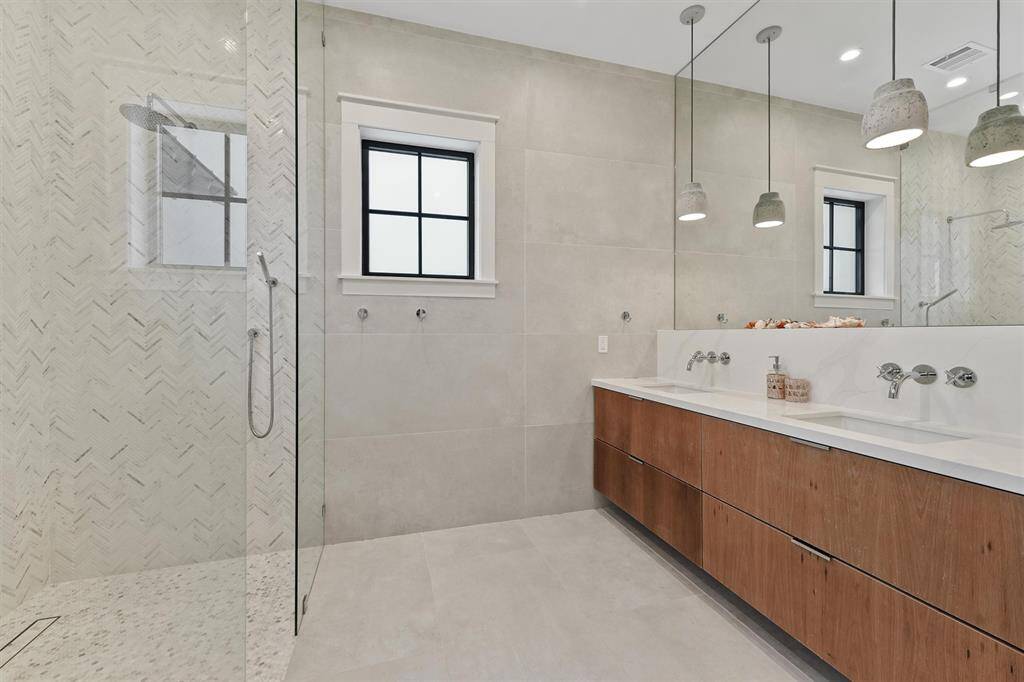 Spacious primary bathroom with a sleek floating vanity, double sinks, and a walk-in rain shower with stunning herringbone tile detail.