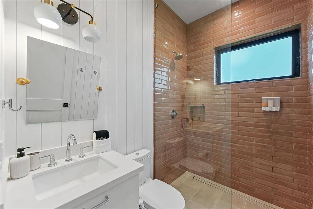 Stylish bathroom with warm-toned subway tile, a sleek glass walk-in shower, and modern gold-accented lighting.