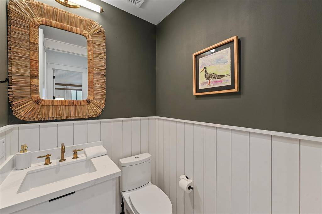 Charming powder room with rich green walls, a coastal-inspired mirror, and elegant gold fixtures.