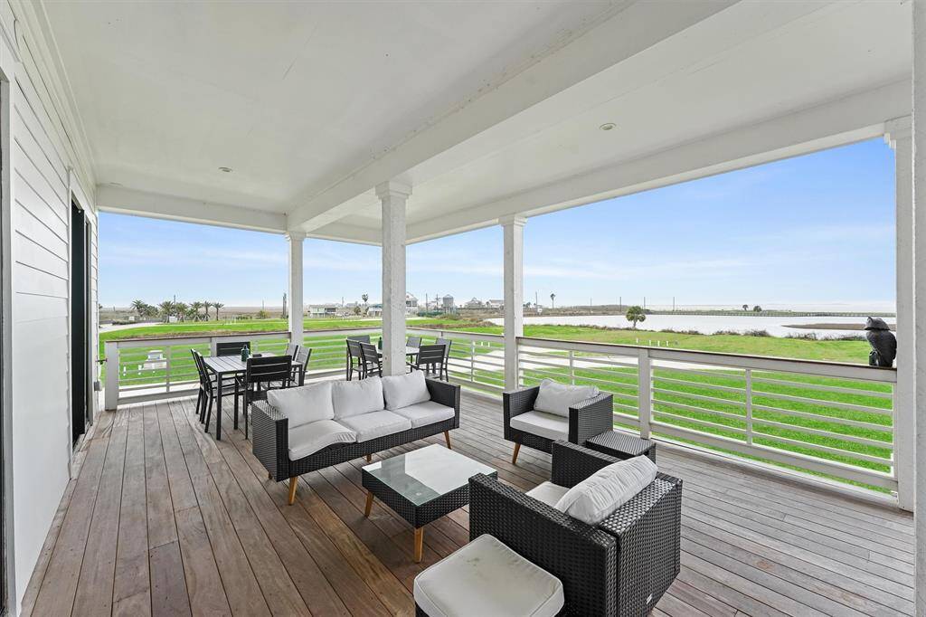Expansive covered deck with comfortable seating and dining space, perfect for enjoying serene bay views and coastal breezes.
