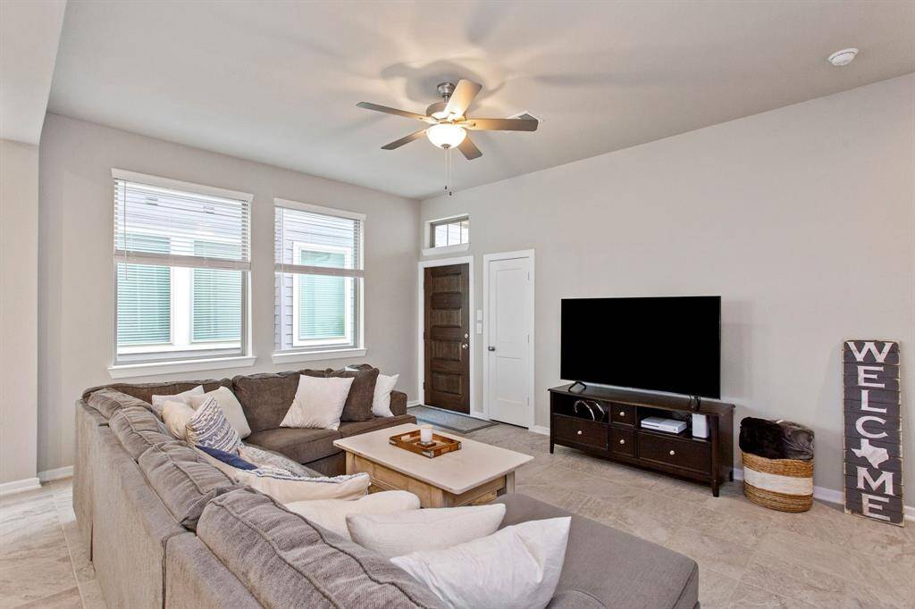 Bright and inviting living room featuring a cozy sectional sofa, large windows for natural light, and a ceiling fan. The space has a modern TV setup and a welcoming decor, perfect for relaxation and entertainment. ( furniture not included, from previous listing )