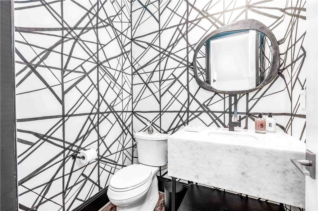 Powder room with a striking black-and-white geometric wallpaper. Contemporary sink with thick marble surround. The design is bold and stylish, offering a unique aesthetic appeal.