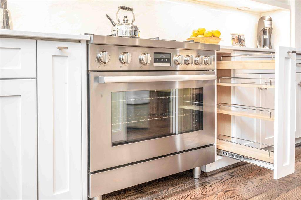 This kitchen features a modern stainless steel BOSCH appliances. It is flanked by cabinetry, including a convenient pull-out pantry for easy storage. The space is bright and well-organized, with hardwood flooring adding warmth.