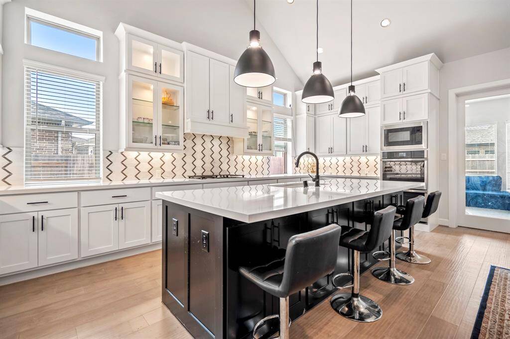 The kitchen boasts a deco wood paneled island with extra cabinets and storage in the front! Upgraded with built-in stainless steel appliances, a 5 burner gas cooktop, and sleek white cabinets with extended upper cabinets and glass panels, this stunning kitchen is ideal for cooking for the whole family or hosting holidays!