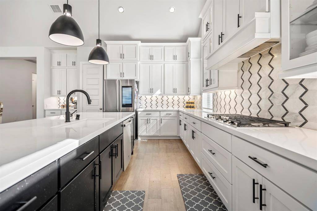 You will love the details of this kitchen! It features under cabinet lighting, a large single basin sink with sleek faucet, modern pendant lights, black cabinet hardware, recessed lighting, quartz counters, splendid textured backsplash, and SS appliances.