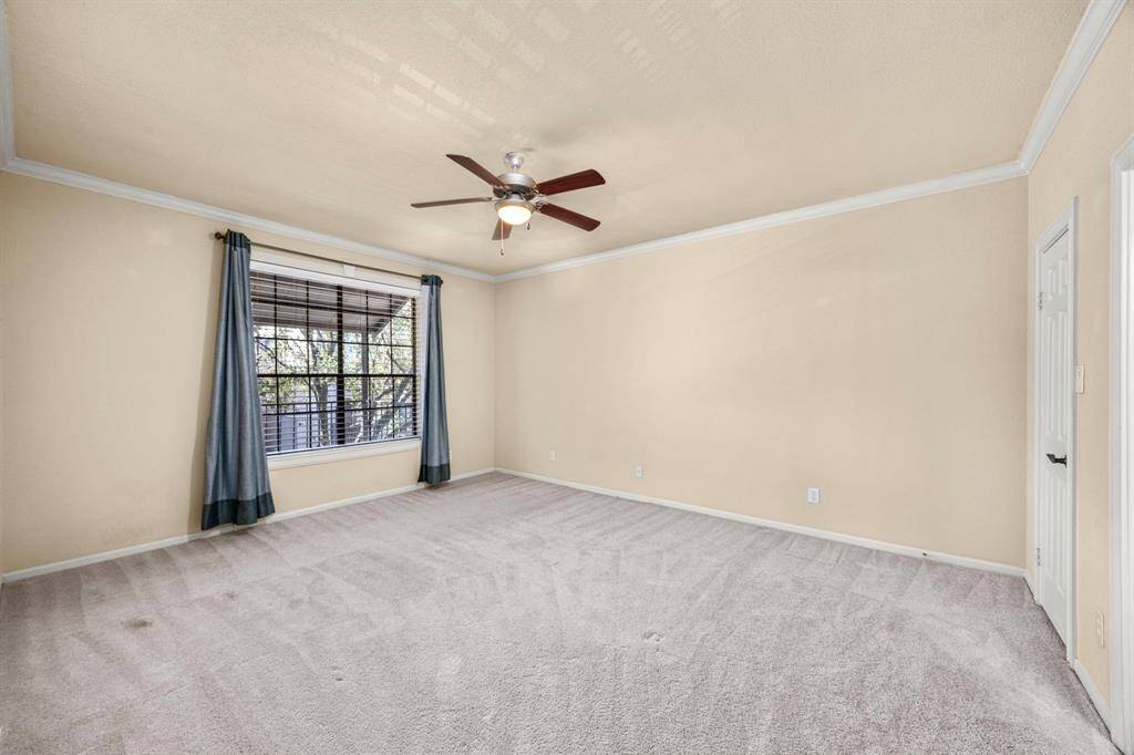 Primary bedroom features plush carpeting, neutral tones, crown molding, a ceiling fan with lighting, and a large window that brings in plenty of natural light.