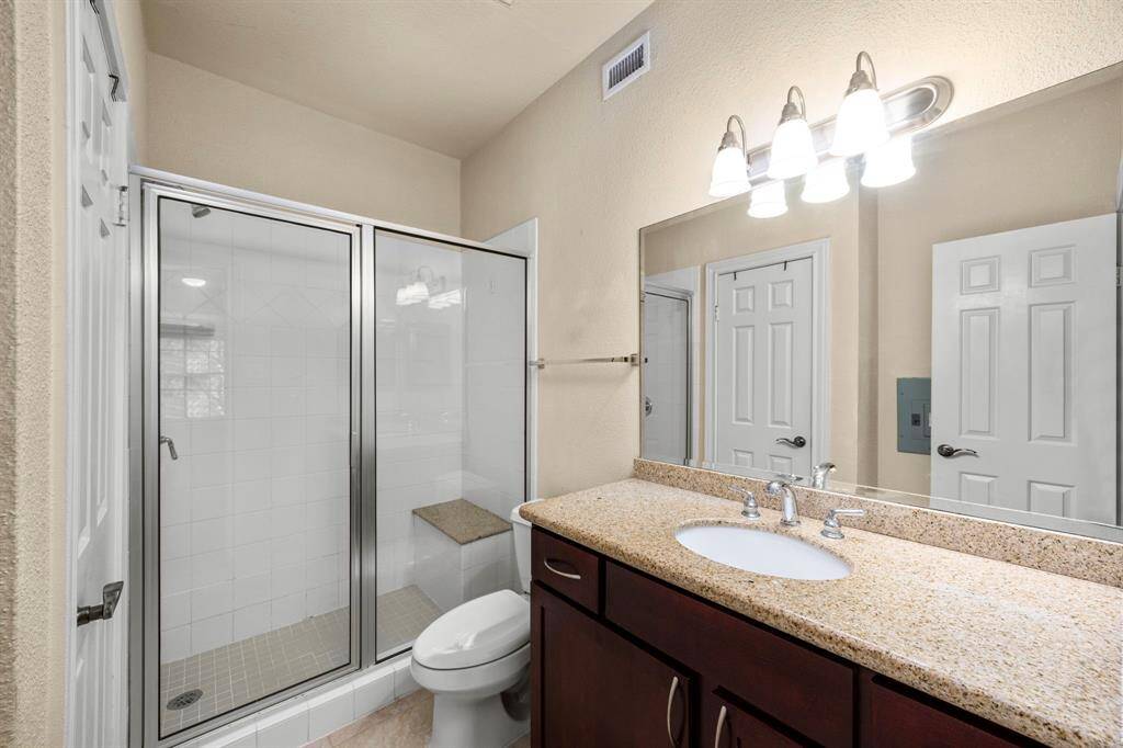 Primary ensuite bathroom features a granite vanity, dark wood cabinetry, a spacious glass-enclosed shower with a built-in bench, and elegant lighting.