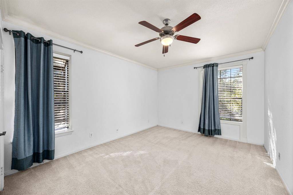 Spacious secondary bedroom features plush carpeting, 2 closets, large windows with natural light, a ceiling fan, and elegant crown molding.