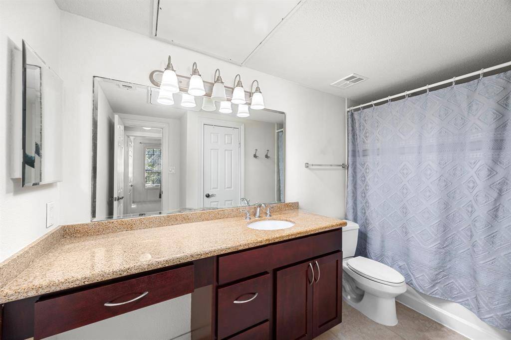 Stylish secondary bathroom features a spacious vanity with granite countertops, rich wood cabinetry, a large mirror with modern lighting, and a full bathtub with a shower.
