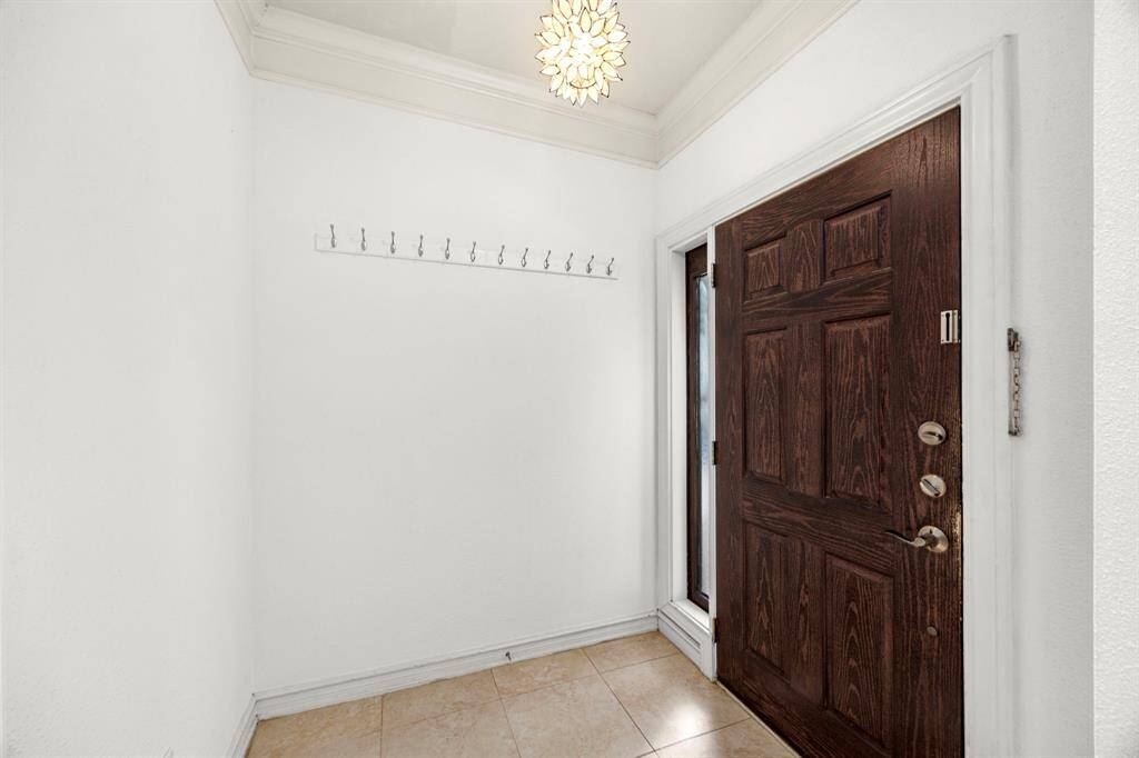 This welcoming entryway features a rich wooden door, elegant crown molding, and a modern light fixture, creating a bright and inviting first impression.
