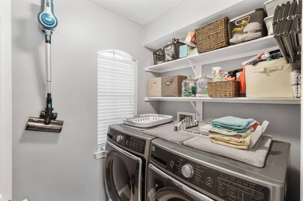 An indoor laundry room offers space for oversized washer and dryer units as well as open shelving for storage.