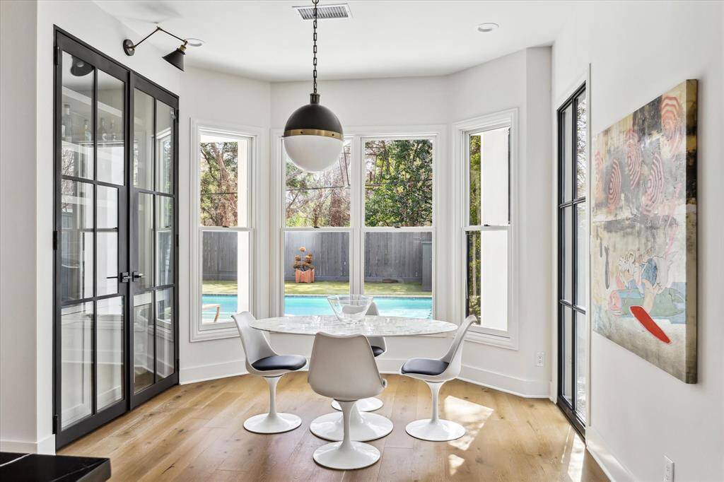 This bright and airy breakfast room features floor-to-ceiling windows with serene pool views, while a sleek dry bar is tucked behind stylish steel and glass doors for effortless entertaining. Chic Thomas O'Brien and LNC lighting give the room a designer touch.