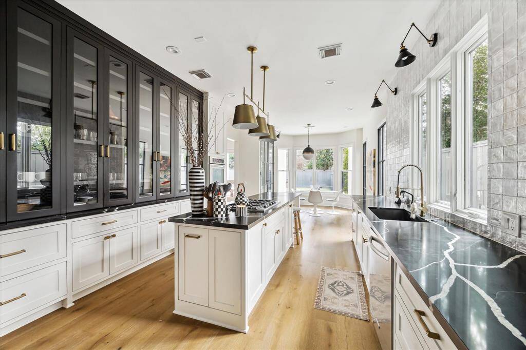 The kitchen offers a perfect balance of style and functionality, featuring custom cabinetry, black quartzite countertops, and a stunning Zellige tile backsplash. High-end KitchenAid appliances and elegant lighting complete the space.