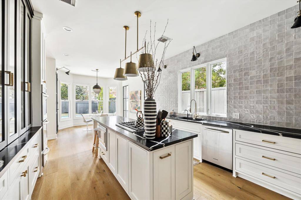 A large island, brass pendant lighting, and a stunning Zellige tile backsplash elevate the kitchen's modern aesthetic, while large windows flood the space with natural light.