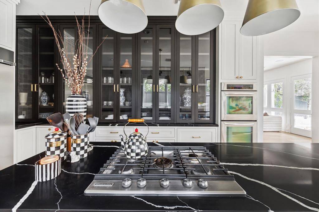 Showcasing bold black glass cabinetry, brass hardware, and a striking gas cooktop on black marble countertops, the kitchen exudes elegance and functionality. Ample storage and refined finishes complete the design.
