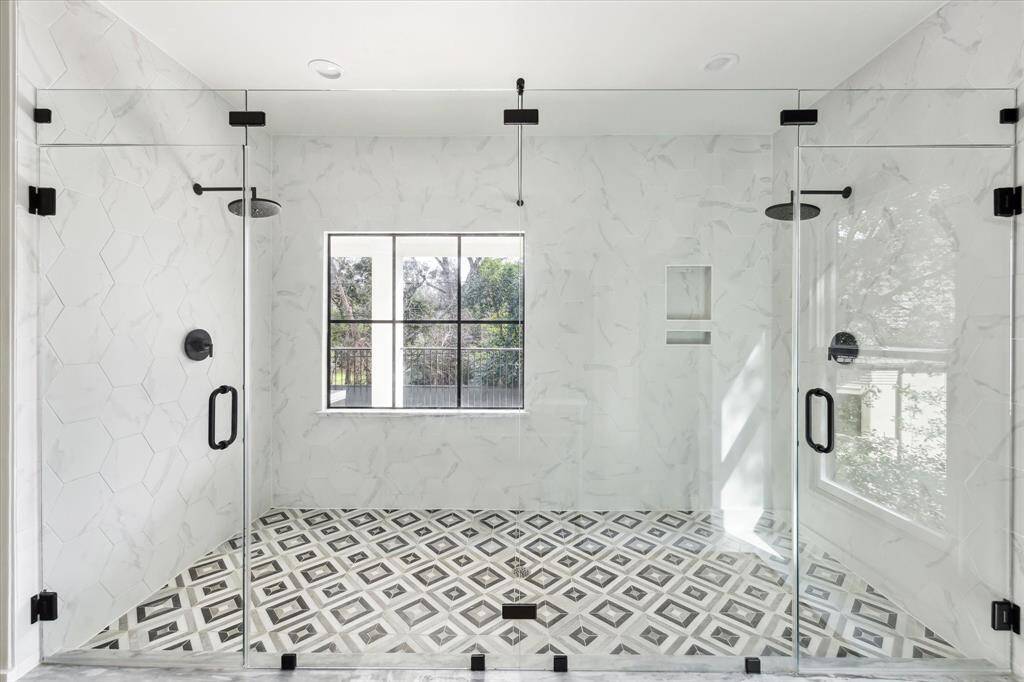 Step into luxury with this expansive glass-enclosed shower, featuring Calacatta marble trim, sleek hexagonal tiles, and dual rainfall showerheads for a spa-like experience.