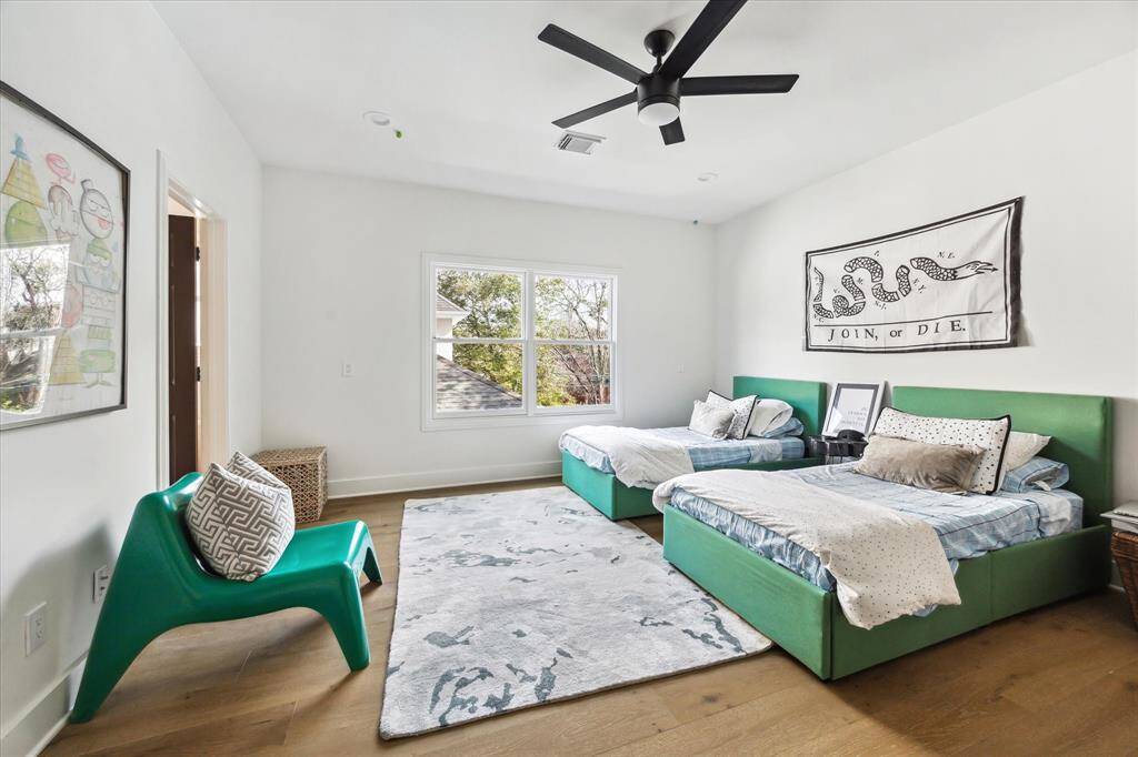 This spacious secondary bedroom features bright natural light, hardwood floors, and a modern ceiling fan, offering a stylish and comfortable retreat.