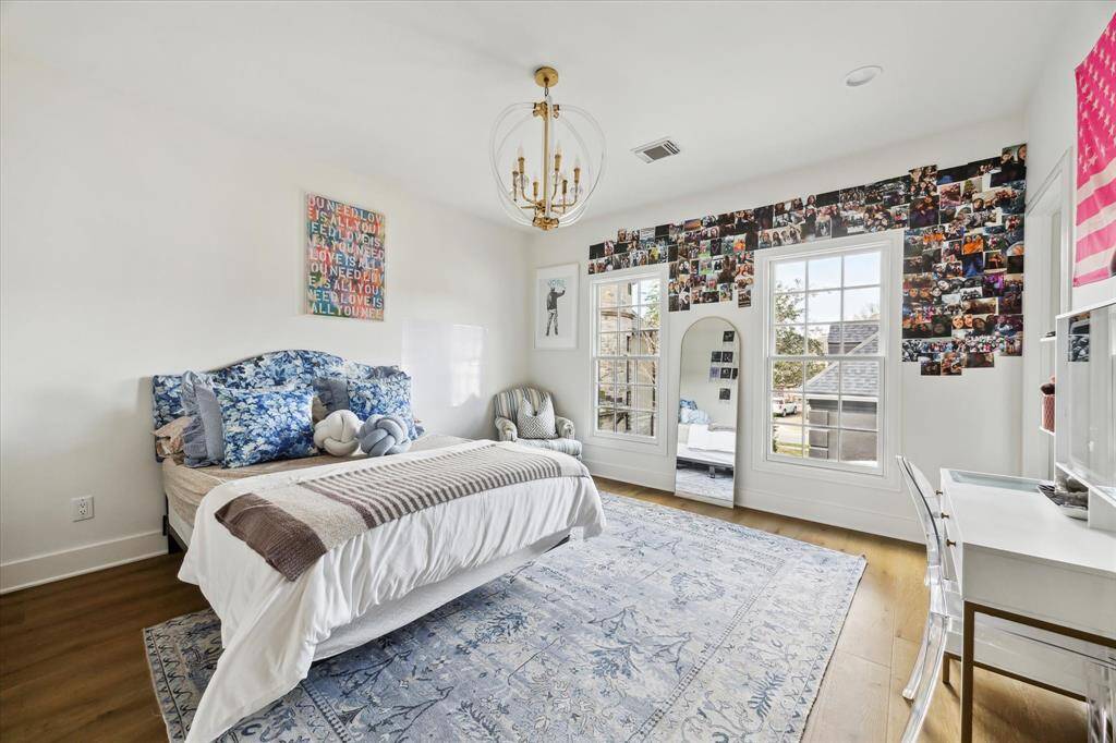 This charming secondary bedroom boasts oversized windows, elegant hardwood floors, and a statement chandelier, creating a bright and stylish retreat.
