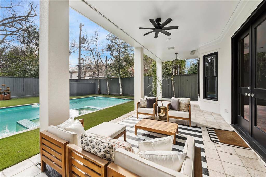 An inviting covered porch offers a seamless indoor-outdoor flow, featuring stylish seating, a ceiling fan, and serene views of the pool—perfect for year-round relaxation.