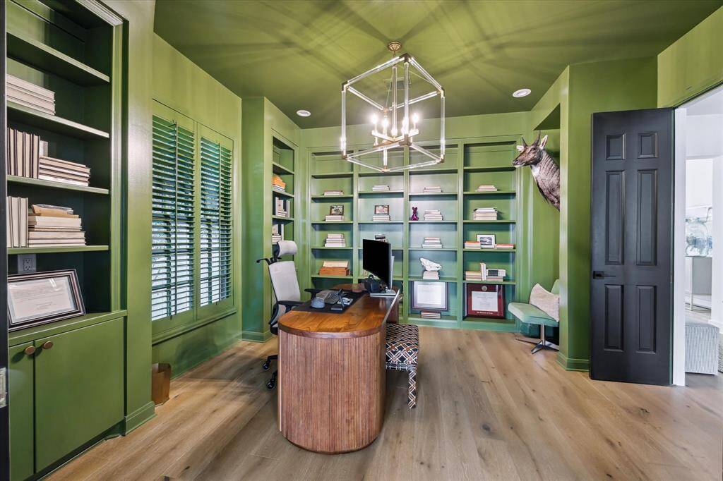 Designed with productivity and style in mind, this home office features striking custom built-ins, rich green paneling, and elegant finishes. Large windows with plantation shutters provide natural light, creating an inspiring and functional workspace.
