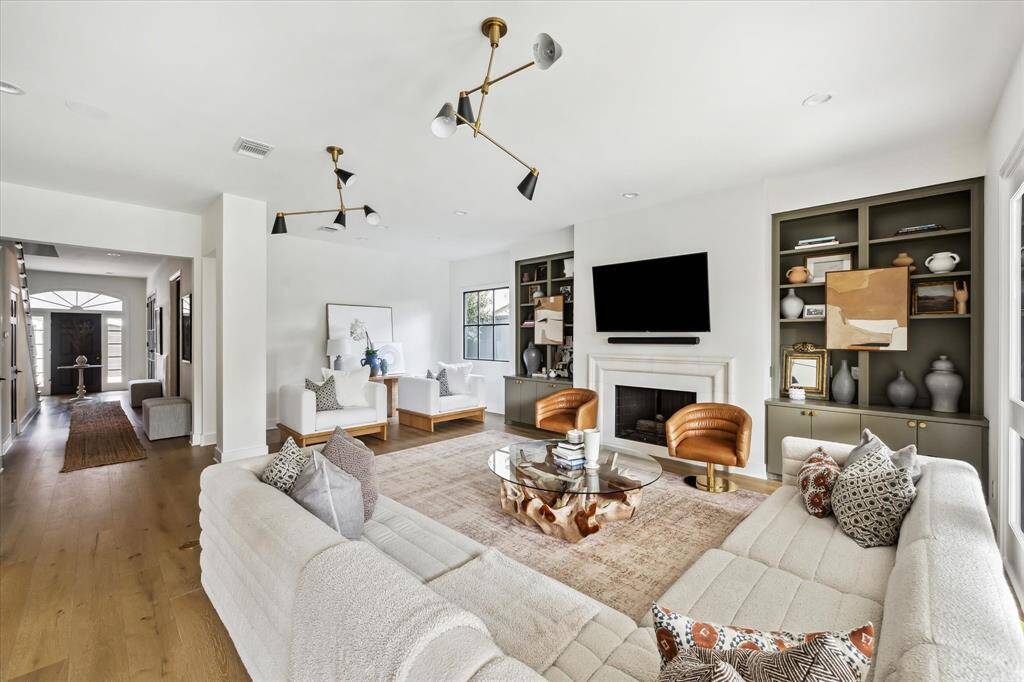 Featuring custom built-in shelving, a sleek fireplace, and 2 stunning Thomas O'Brien chandeliers, the spacious family room offers an open layout that seamlessly connects to adjoining spaces, ideal for entertaining and everyday living.