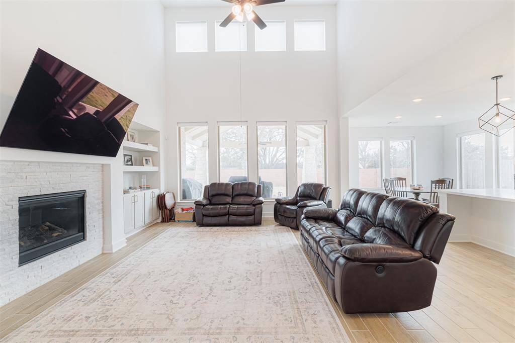 The spacious family room showcases soaring ceilings, a wall of windows, a stone-surround gas-log fireplace, and built-ins.
