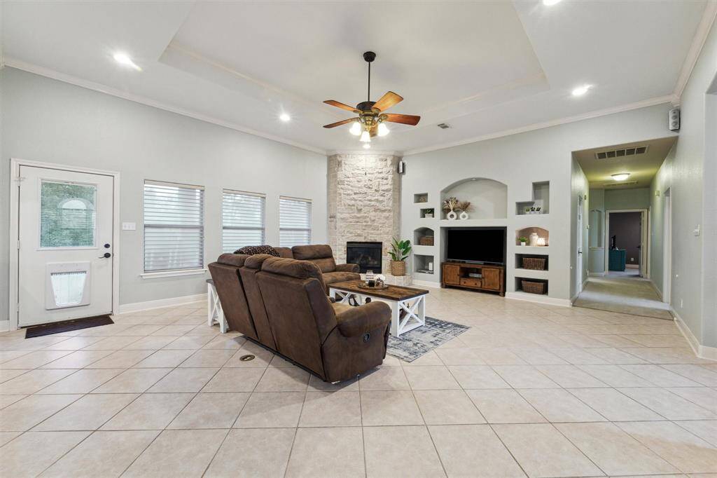 The large living room with a stone gas-log fireplace, crown molding, tray ceiling and recessed lighting.