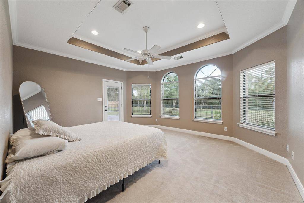 The spacious primary suite looks out over the backyard with a door to the covered patio. Notice the tray ceiling, crown molding and recessed lighting.