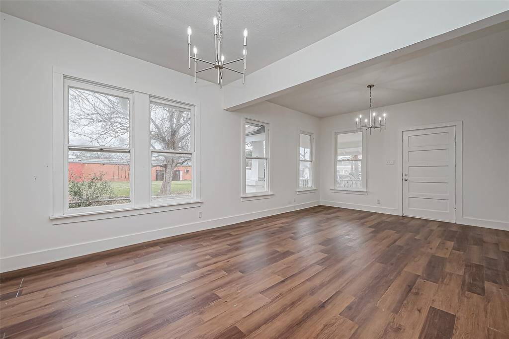 Stepping inside, the spacious living room is bathed in natural light from large windows, highlighting the contrast between crisp white walls and gleaming new floors. Stylish chandeliers add a touch of character, while the open layout connects seamlessly to the dining area, offering plenty of space for gathering and daily living.