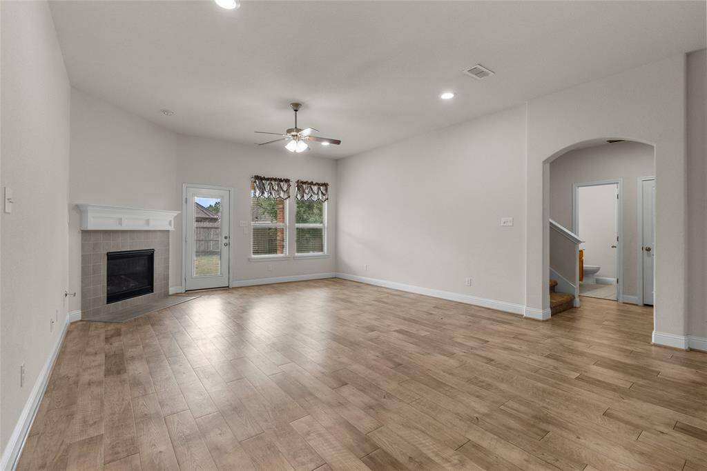 This spacious, well-lit living room featuring a modern fireplace, elegant wood look flooring, and large windows with backyard views. The room has neutral color palette, ready for your personalization.