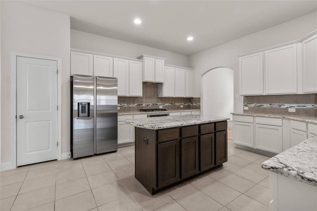 This extra large Modern kitchen featuring stainless steel appliances, ample white cabinetry, granite countertops, and a central island with contrasting dark cabinetry. The space is complete with tiled flooring and a neutral color palette, ready for personal touches.