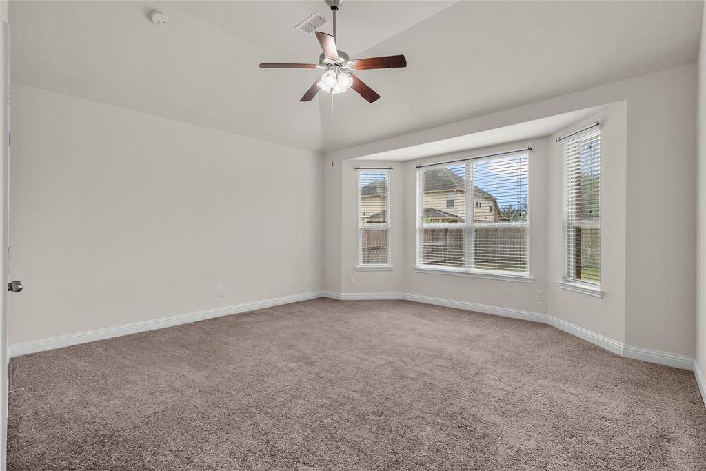This is a spacious Primary Suite well-lit room with neutral walls and carpeting, featuring a ceiling fan and multiple windows offering natural light.