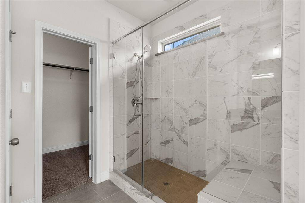 This is a modern bathroom featuring a spacious walk-in shower with elegant marble-like tile and a glass seamless door, with a huge bench in the shower