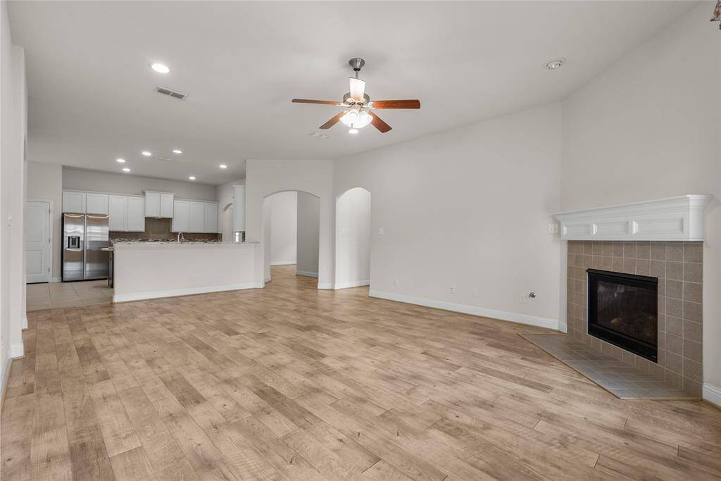 This spacious open-concept living area featuring wood look flooring, a modern kitchen with stainless steel appliances, ample cabinetry, and a central island. The room is well-lit with recessed lighting and includes a ceiling fan and a fireplace with a traditional mantel. This area is huge for having gatherings