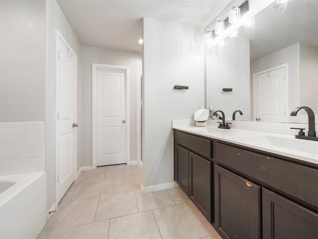 This spa-like retreat features a dual vanity with sleek black fixtures, a soaking tub, and a separate walk-in shower. With ample storage and a spacious layout, this en-suite bath offers both comfort and elegance.
