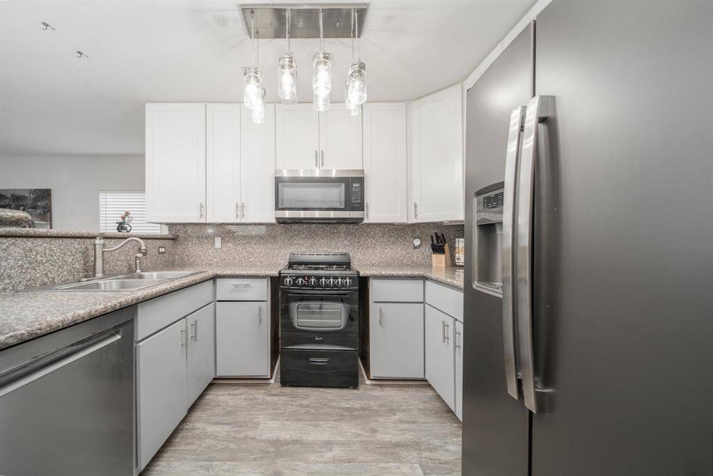 Cozy and beautiful, this remodeled kitchen rests under a collection of elegant drop lights. Stainless steel appliances, including the refrigerator, finish this space perfectly.