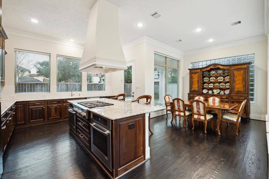 Also included in the Kitchen are stained wood drawers/cabinets, stained planked wood flooring, granite counters, under-cabinet lighting, ceramic dual basin sink, white subway tile backsplash, stainless Jenn Air refrigerator, stainless Jenn Air dishwasher, glass front doors to covered outdoor patio and backyard garden, crown/base molding, recessed lighting, three oversized windows with blinds.