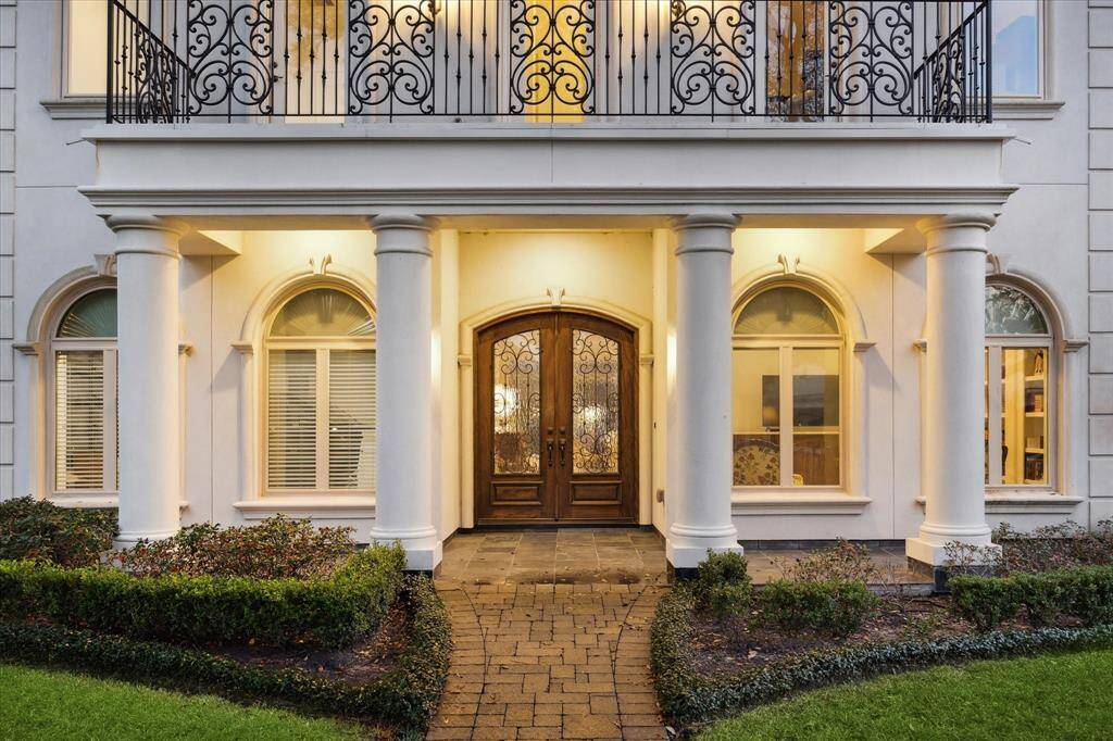 Sophisticated French stucco facade design as seen in the brick paver walkway, painted columns supporting the Front double Door/Porch with balcony above and its noteworthy delicate decorative wrought iron railing. All balanced by a series of oversized windows with arched transoms above, decorative quoins at facade corners and all surrounded by the expansive front yard with manicured shrubbery beds.