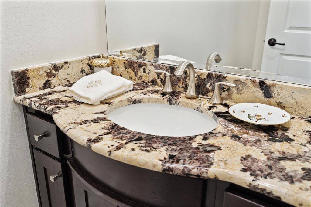 The Back Hallway Powder Room is appointed with granite counter/backsplash, furniture style sink with stained cabinets/drawers below, tile flooring, mirror with light sconce, base molding, painted walls.