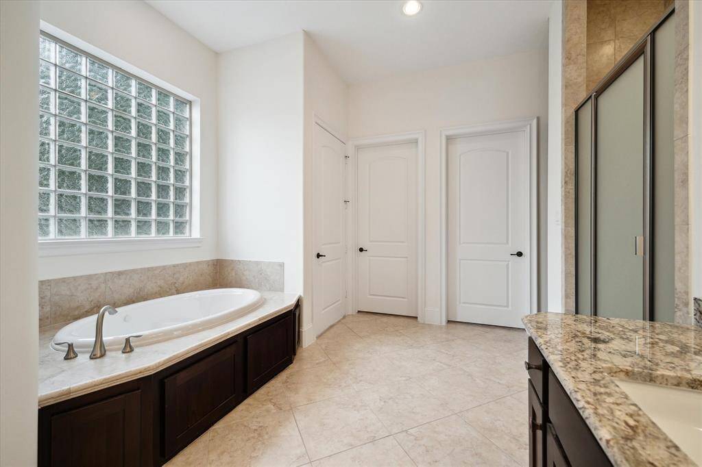 Closer view of the Primary Bath showing the spa tub with tile surround and glass block window.  Additionally seen is the walk-in shower with with frosted glass door/tile surround/built-in bench, and the dual closets entry doors.