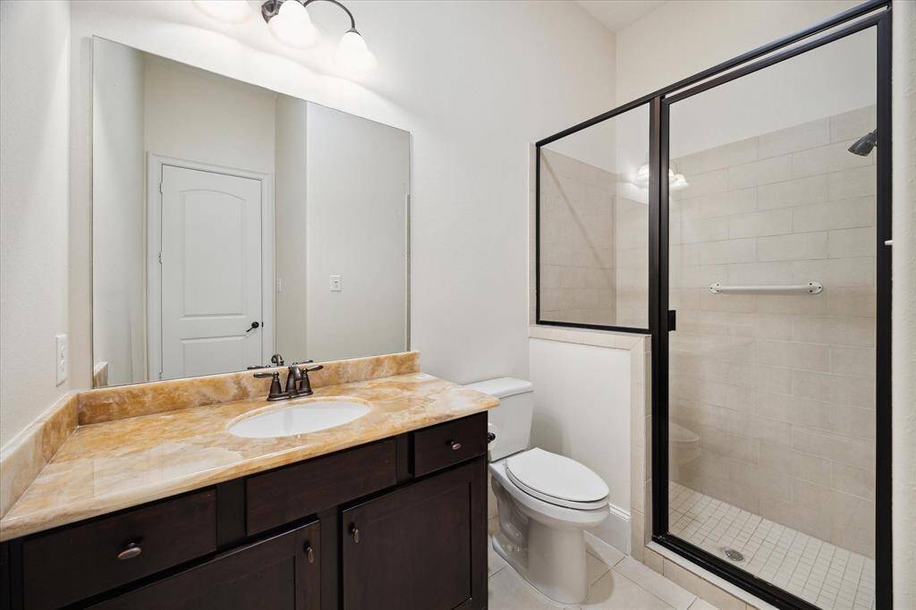EN SUITE BATH to downstairs Guest Bedroom features tile flooring, onyx slab counter with cabinets/drawers below, mirror with light sconce, glass front walk-in shower with tile surround/flooring.